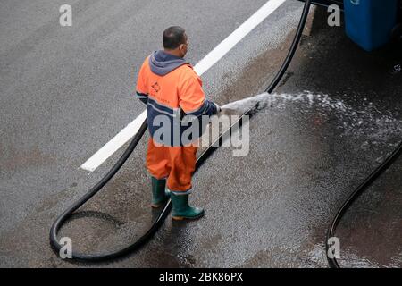 Belgrado, Serbia - 24 aprile 2020: Lavoratore in uniforme arancione lavando la strada con tubo dell'acqua, vista posteriore ad angolo elevato; Foto Stock