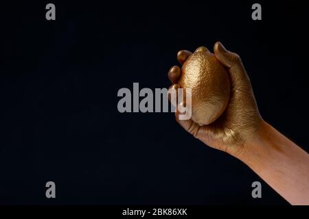 Concetto di minimalismo. Mano tiene limone in vernice oro Foto Stock