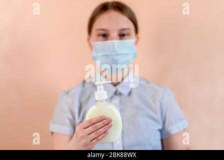 Una ragazza adolescente di 12-15 anni, in una maschera medica copre il suo viso, tiene un antisettico in mano, sapone liquido, cura e aiuto ricordare ai pazienti Foto Stock