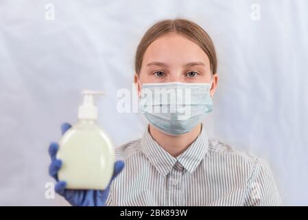 adolescente ragazza, in maschera medica copre il suo viso, tiene antisettica la sua mano, sapone liquido, sfondo bianco, assistenza ricordare ai pazienti circa la sicurezza Foto Stock