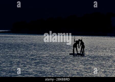 Coppia pagaia sulle tavole di sup sul mare durante il tempo al chiaro di luna Foto Stock