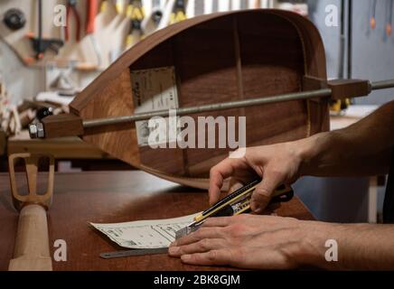 una scena closeup delle mani di liutaio che tagliano i titoli fatti a mano per gli strumenti musicali di legno Foto Stock