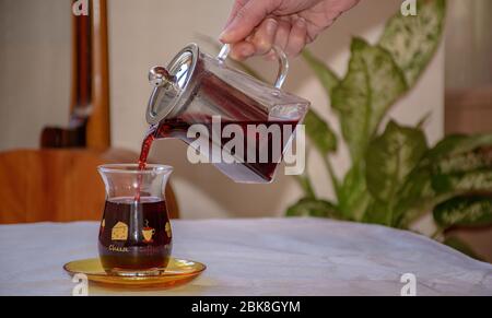 femmina mano che versa il tè di ibisco in un classico bicchiere turco, primo piano Foto Stock