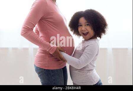 Eccitata piccola ragazza nera coccolando il ventre incinta di sua madre Foto Stock