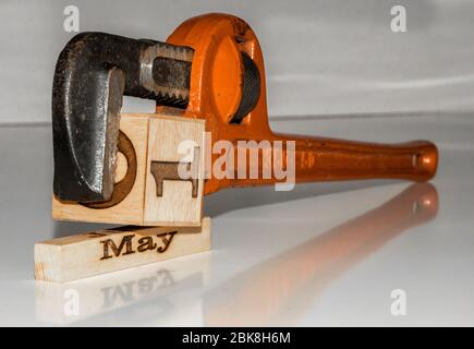 una chiave per tubi che comprime il cubo di legno 'primo di maggio' - tema del giorno del lavoro con cubi / blocchi di calendario in legno Foto Stock