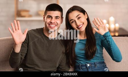 Coppia seduta sul divano a casa e ondeggiante alla macchina fotografica Foto Stock