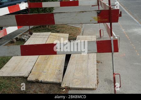 piccolo albero di ingegneria civile coperto da tavole di legno, bordato da una recinzione fatta di tavole di barriera di rosso e bianco su un marciapiede Foto Stock