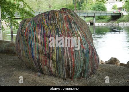 una grande pietra sulla riva del fiume coperta da sottili strisce di vari colori. Una decorazione astratta di un masso indipendente con un contorno di un ponte Foto Stock