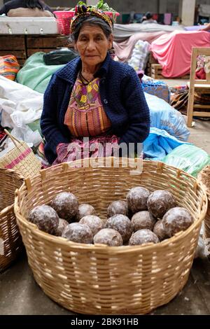 Donna vestita con abiti indigeni colorati che vendono frutta in un mercato locale. Foto Stock