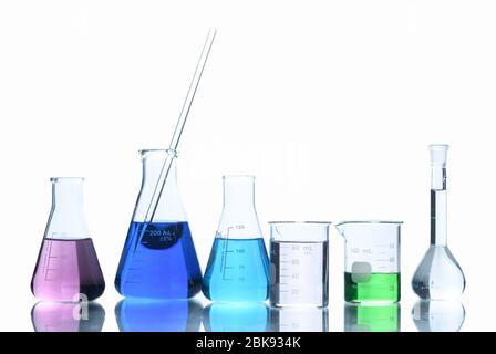 Vetreria da laboratorio con liquidi di diversi colori, matracci e becher di misurazione per esperimenti scientifici in laboratorio isolato su sfondo bianco A. Foto Stock
