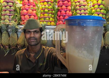 Presso la famosa Badshah Cold drink House nella zona di Crawford Market, Mumbai, India, un dipendente prepara un Chikoo Milkshake, mucchi di frutta in b/g. Foto Stock