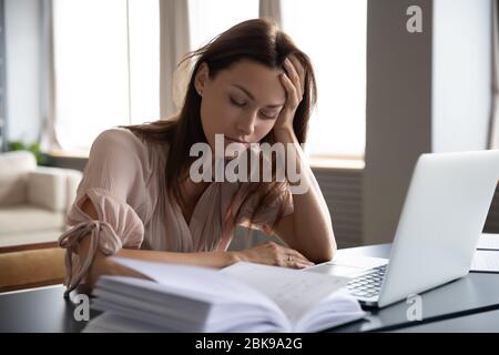 Donna stanca e sonnolenta seduta alla scrivania con notebook, con testa in mano Foto Stock