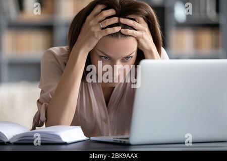 Donna stressata e infelice che guarda lo schermo del notebook, che tocca la testa Foto Stock