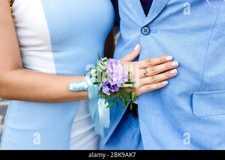 Giovane donna con una boutonniere floreale su una mano in un abito blu abbracciando un uomo in un vestito blu Foto Stock