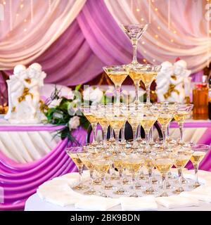 Piramide di bicchieri con champagne in interni viola per matrimoni. Foto Stock