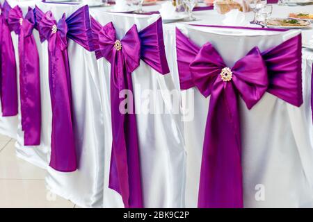 sedie decorate con archi viola alla cerimonia Foto Stock