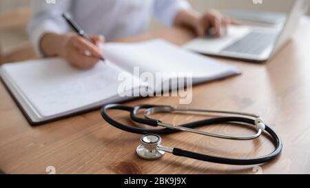 Medico femminile che usa il laptop, scrivendo note con stetoscopio sul tavolo Foto Stock