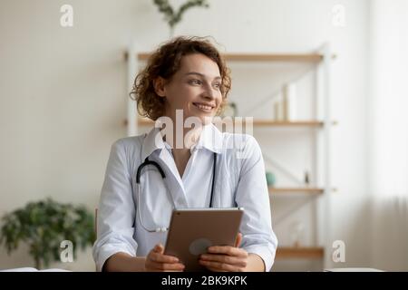 Giovane donna sorridente professionista medico che tiene un tablet digitale guardare lontano Foto Stock