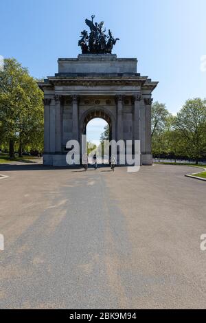Lockdown London: Tre ciclisti pedalano attraverso il Wellington Arch su Hyde Park Corner, che un tempo conteneva la più piccola stazione di polizia di Londra. Foto Stock