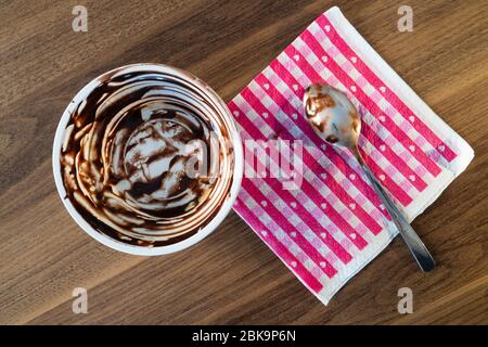 Un piatto di profiterole da dessert vuoto e un tovagliolo di carta rossa con cucchiaio su un tavolo di legno marrone dopo essere stato mangiato Foto Stock