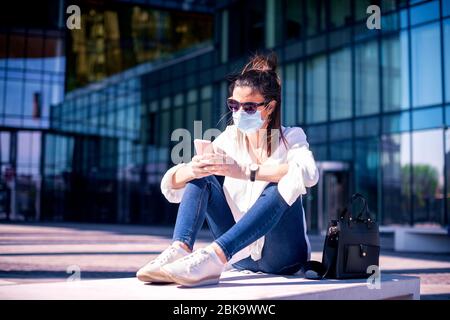 Scatto a lunghezza intera di donna d'affari caregata che indossa la maschera facciale per la prevenzione e la messaggistica di testo mentre sulla strada. Foto Stock