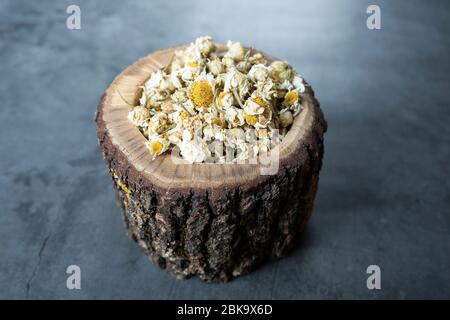 Tè alla camomilla essiccato in ciotola di legno su pietra, fondo in cemento. herbals secco, organico, sano e rilassante. Foto Stock