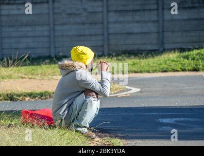 Alberton, Sudafrica - uomo nero non identificato siede su un angolo della strada durante la chiusura nazionale in attesa di un handout o di un lavoro part-time Foto Stock