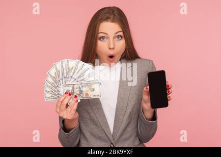 Domanda online, domanda di prestito. Ritratto di donna d'affari stupita in giacca vestito con banconote in dollari e cellulare, scioccato da mobile banking. ind Foto Stock