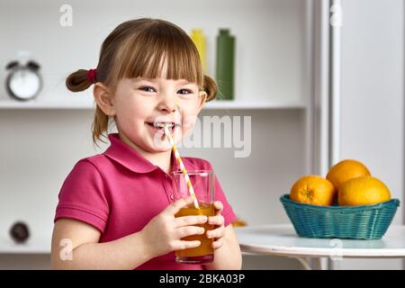 La bambina carina beve succo d'arancia a casa. Foto Stock