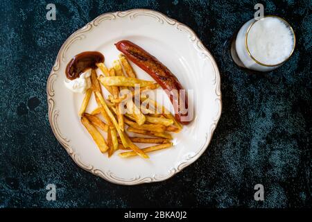 Salsiccia fatta in casa con patate Skinny French Fries in piatto con bicchiere di birra anche chiamato Peruvian Salchipapa. Fast food. Foto Stock