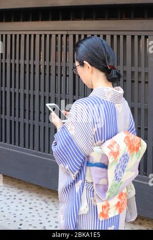 Donna giapponese in kimono che controlla il suo smartphone mentre cammina Foto Stock