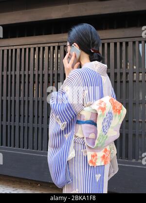 Donna giapponese in kimono che parla sul suo smartphone mentre cammina Foto Stock