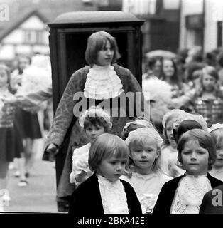 La processione annuale del Knutsford Royal May Day nel 1976 a Knutsford, Cheshire, Inghilterra, Regno Unito. Include tradizionalmente una fantasia-abito pageant di bambini in costumi storici o leggendari con traini a cavallo. Qui i bambini in costume storico camminano nella processione davanti ad un ragazzo adolescente che porta le maniglie anteriori di una lettiera o di una sedia berlina. Foto Stock