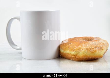 Una deliziosa ciambella rivestita di zucchero si trova tentevolmente accanto a una tazza da caffè da 11 ml. Foto Stock