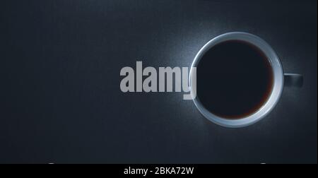Flatlay, vista dall'alto di scuro e di moody illuminato una tazza da caffè con sfondo nero e duro scarsa luce spazio di copia contidion Foto Stock