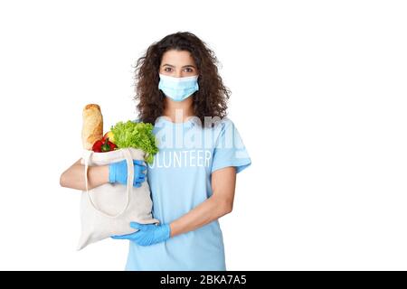 Ragazza ispanica volontario indossare maschera tenere sacchetto con consegna di cibo isolato su bianco. Foto Stock