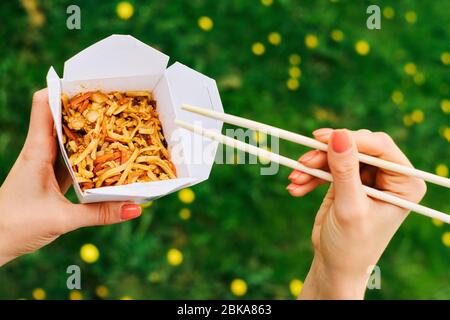 wok noodles con verdure in scatola di cartone per andare, con bacchette di bambù, primo piano Foto Stock