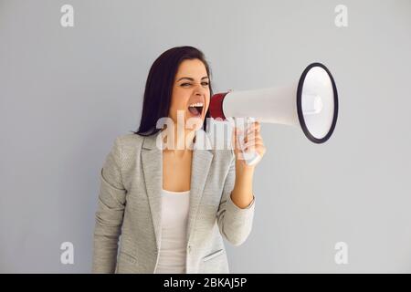 Donna ispanica con un altoparlante grida annuncia la protesta di notizie su uno sfondo grigio. Foto Stock