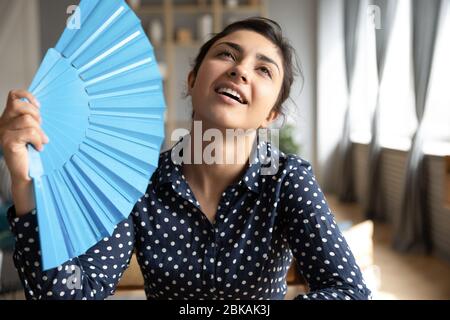 Testa sparato giovane donna indiana utilizzando la carta blu ventilatore. Foto Stock