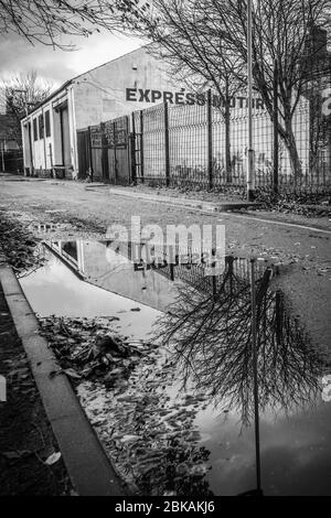 Una vista di un garage disuso nel quartiere post-industriale di Ancoats, nel centro di Manchester, si riflette in una grande pozzanghera su una strada acciottolata. Foto Stock