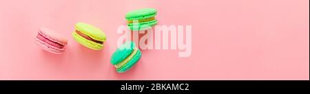 Dolce mandorla colorato rosa blu giallo verde macaron o torta da dessert macaroon isolato su sfondo rosa pastello alla moda. Biscotti dolci alla francese. Concetto di panetteria alimentare minimo. Banner con vista dall'alto piatto Foto Stock