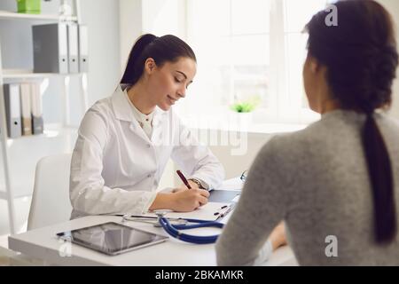 Paziente donna in visita medico femminile presso l'ufficio della clinica. Il lavoro medico scrive una prescrizione su un tavolo in un ospedale. Foto Stock