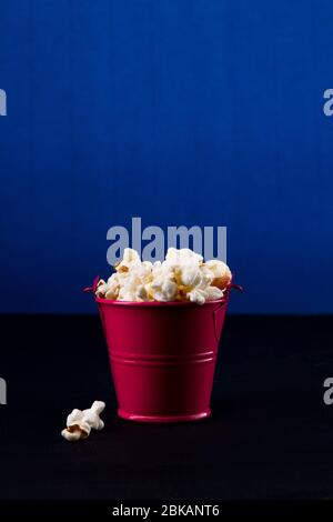 Secchio rosso pieno di popcorn su sfondo blu scuro. Foto Stock