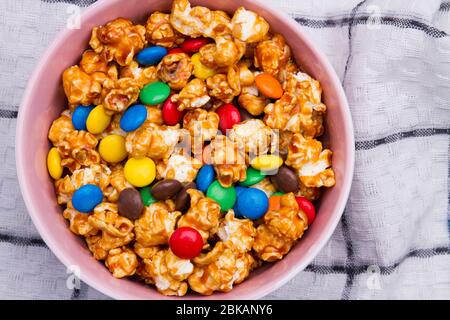 Caramelle al cioccolato e popcorn dorato si mescolano in piastra di ceramica su tovagliolo bianco. Foto Stock