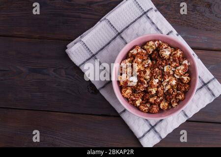 Primo piano il cioccolato ricoperto di popcorn in una ciotola rosa su sfondo di legno scuro. Foto Stock