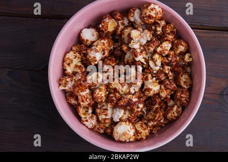 Primo piano delizioso cioccolato ricoperto di popcorn in una ciotola rosa su sfondo di legno. Foto Stock