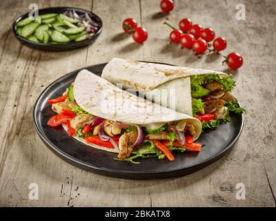 Tortilla si avvolge con carne di pollo fritto e verdure su tavola di legno Foto Stock
