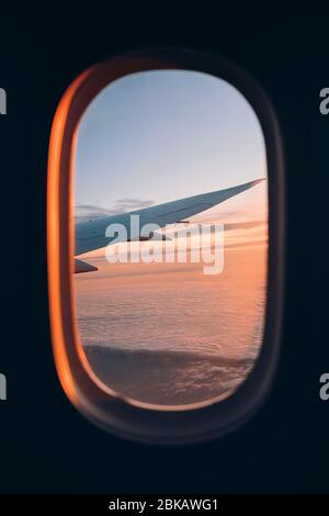 Vista dalla finestra del velivolo durante il volo sopra le nuvole al tramonto. Messa a fuoco selettiva sul parafango. Foto Stock