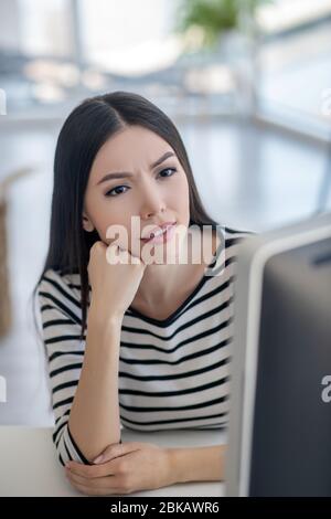 Donna brunetta in camicia a righe ascoltando con attenzione Foto Stock