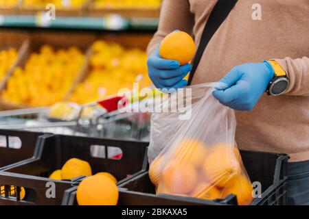 L'acquirente di uomo senza volto sceglie le arance fresche nel centro commerciale, afrids di coronavirus, indossa i guanti di gomma durante lo scoppio del virus, compra i prodotti o il cibo. P Foto Stock